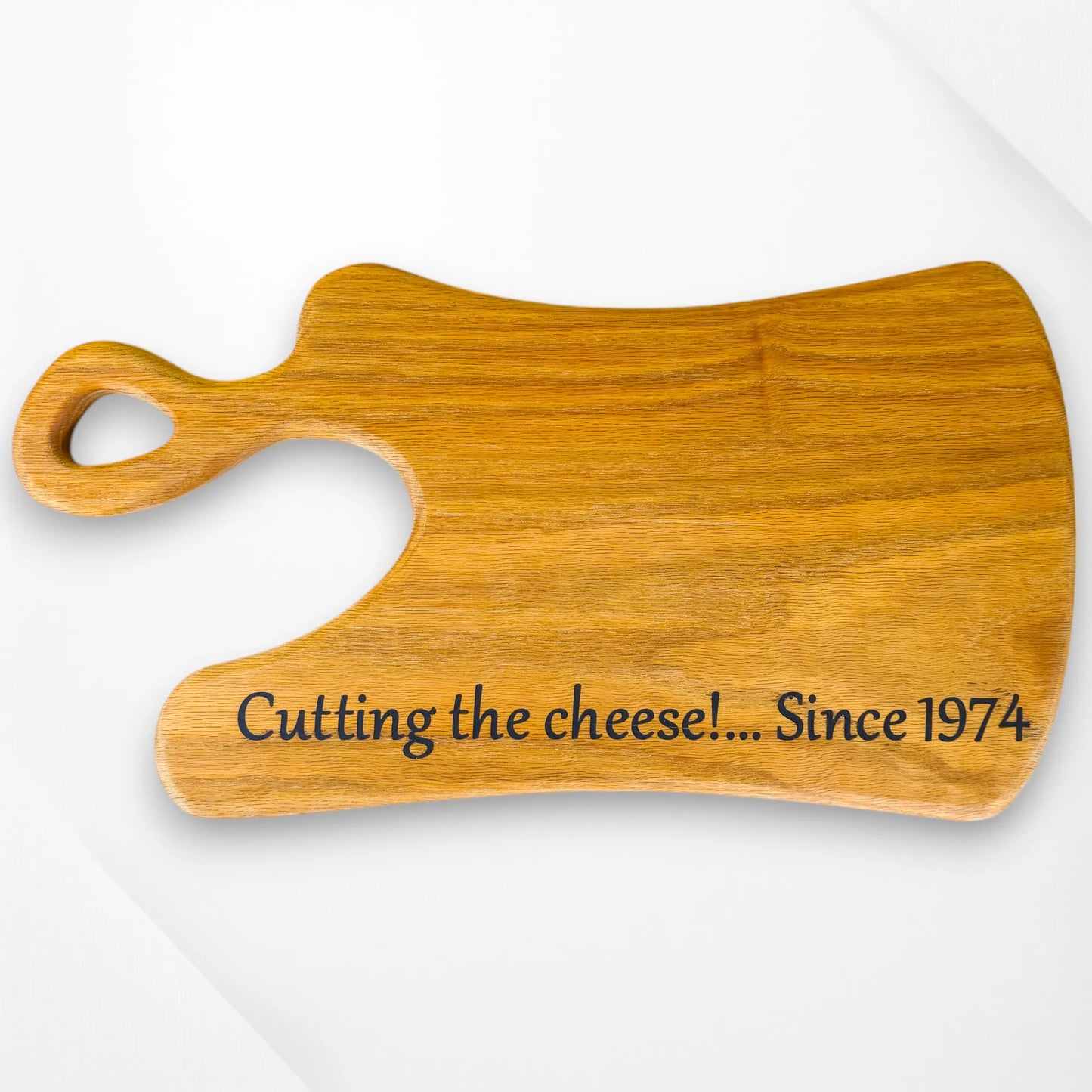Personalised oak cheese board with “Cutting the cheese!... Since 1974” engraved, unique handle design and natural wood grain. Handmade by The Crafty Oak.