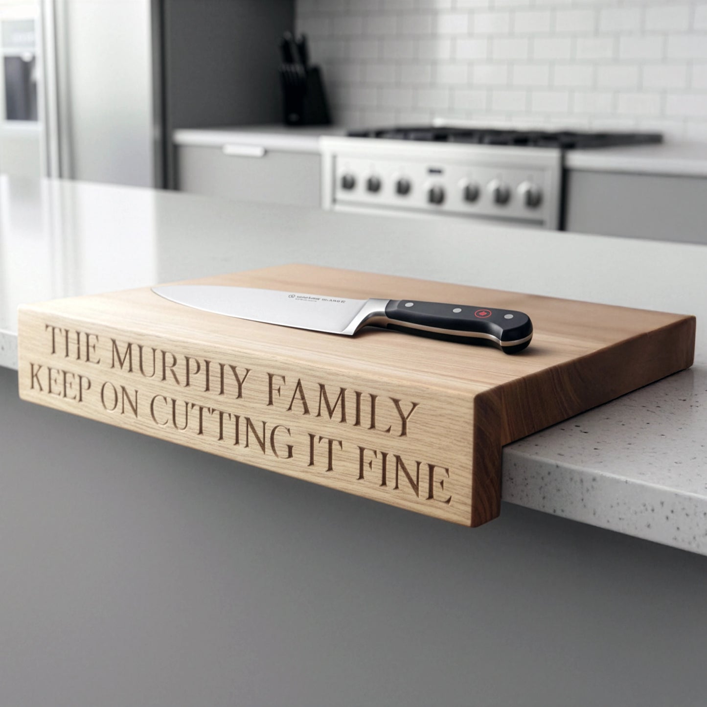 “Personalised oak overhang chopping board engraved with ‘The Murphy Family Keep on Cutting It Fine,’ shown on a modern kitchen worktop with chef’s knife resting flat on top.”