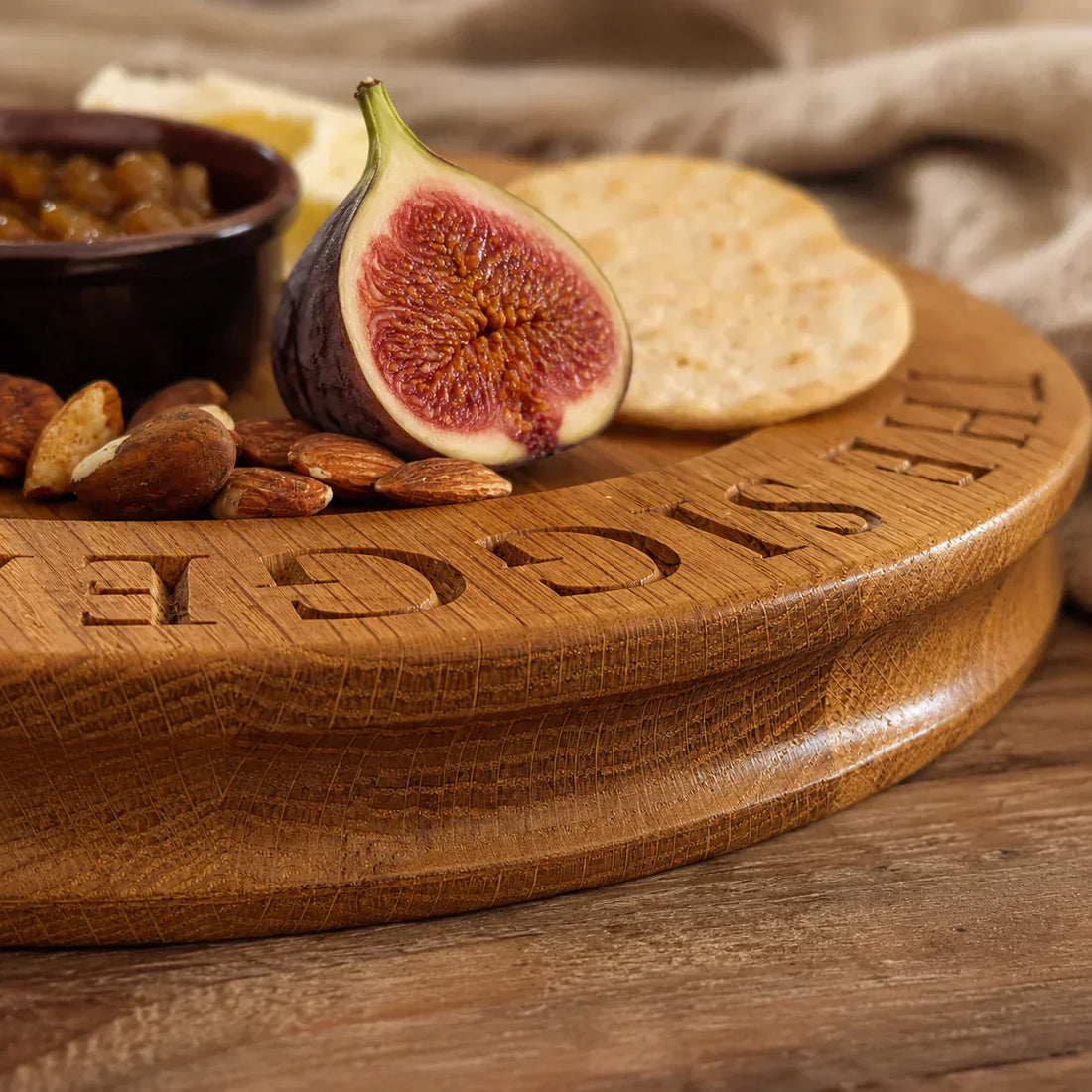 Personalised oak cheese board with carved lettering, fig, crackers and almonds on a rustic wooden table