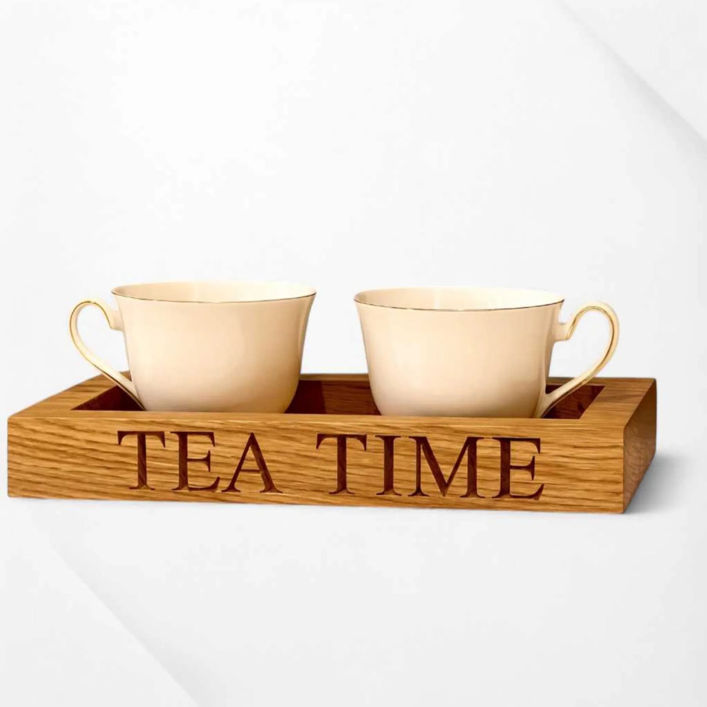A pair of cream-coloured teacups sit inside a handcrafted oak tea tray engraved with the words "TEA TIME" with a clean white background.