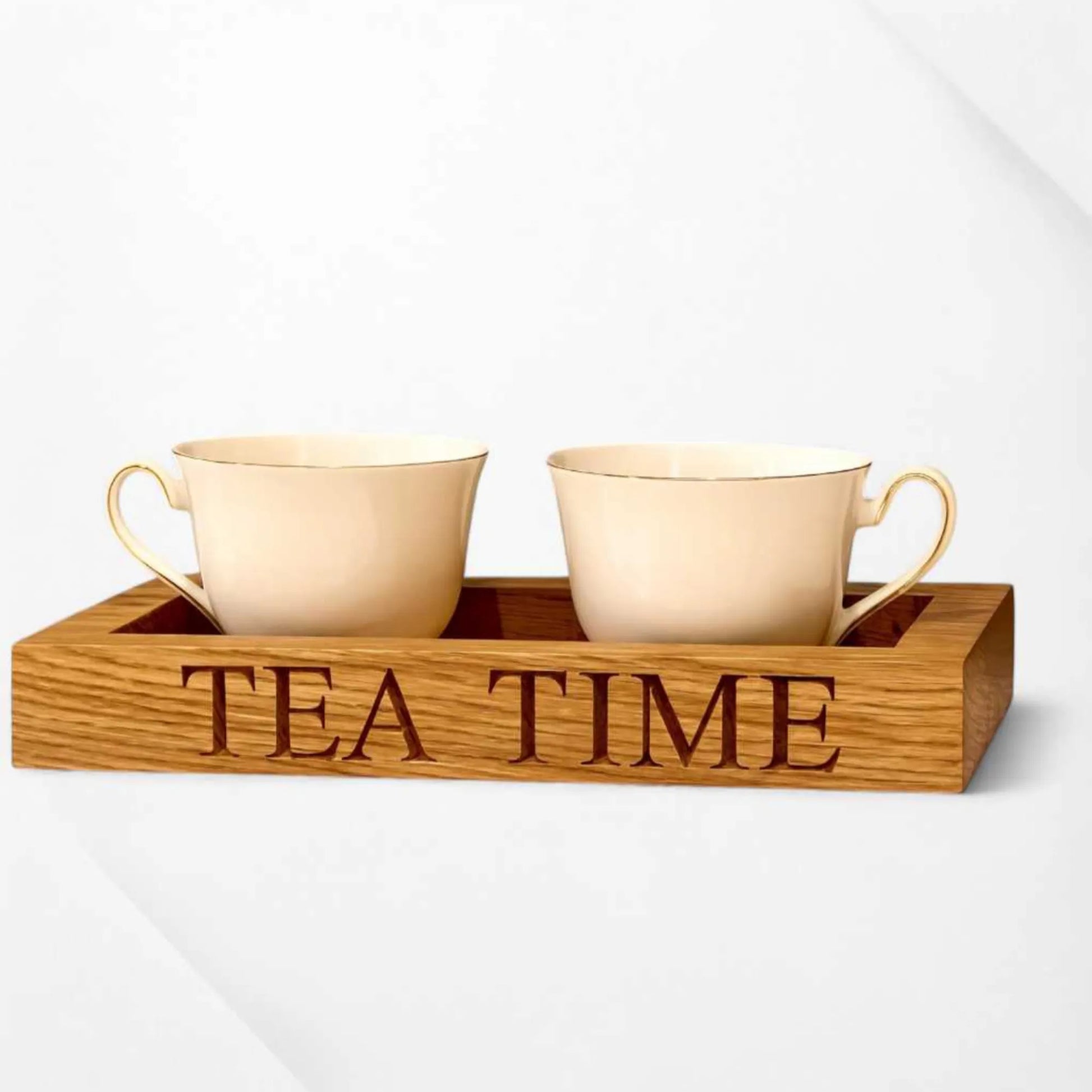 A pair of cream-coloured teacups sit inside a handcrafted oak tea tray engraved with the words "TEA TIME" with a clean white background.