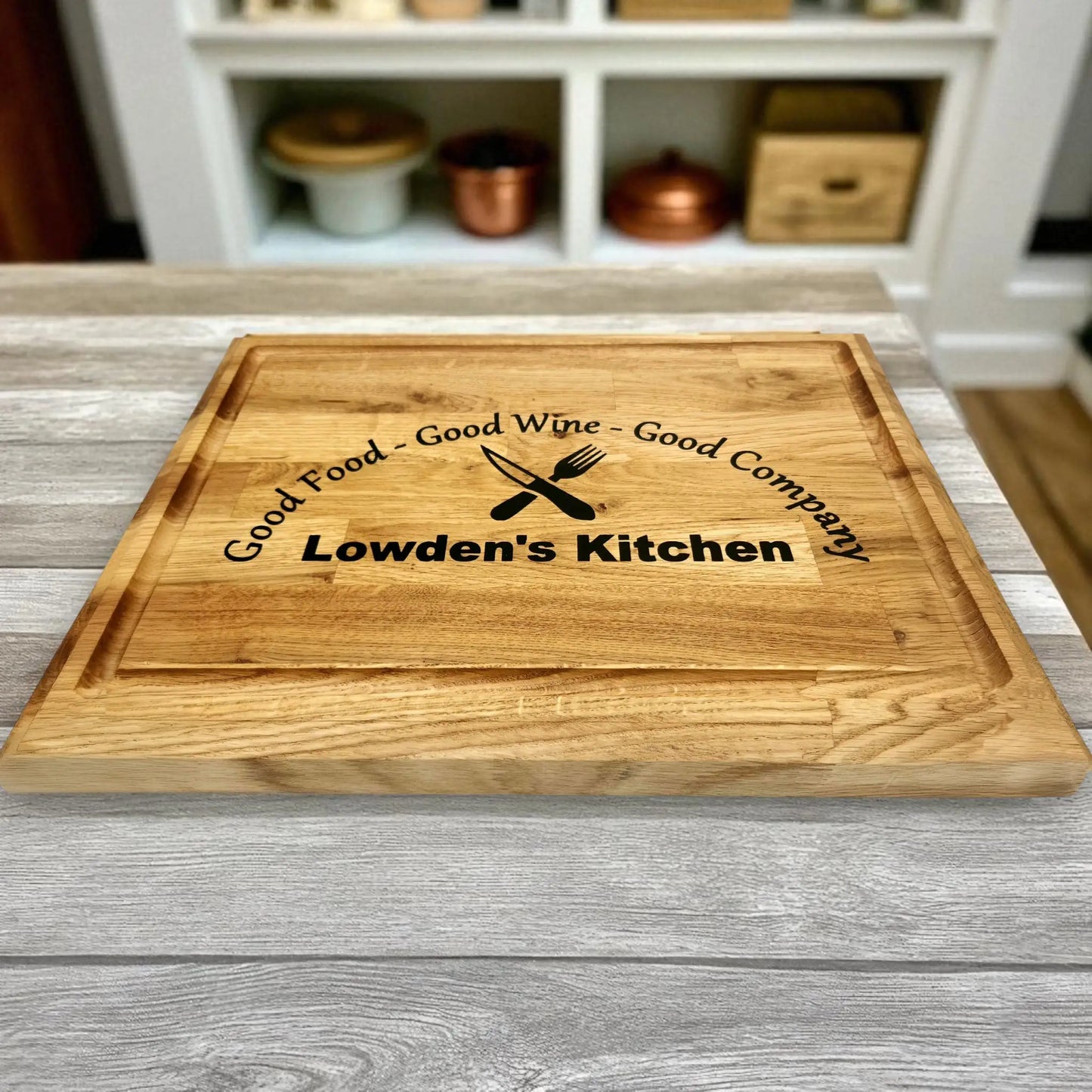 Personalised oak chopping board engraved with the phrase ‘Good Food – Good Wine – Good Company’ and custom name ‘Lowden’s Kitchen,’ displayed on a rustic kitchen counter, ideal gift for home chefs or family kitchens