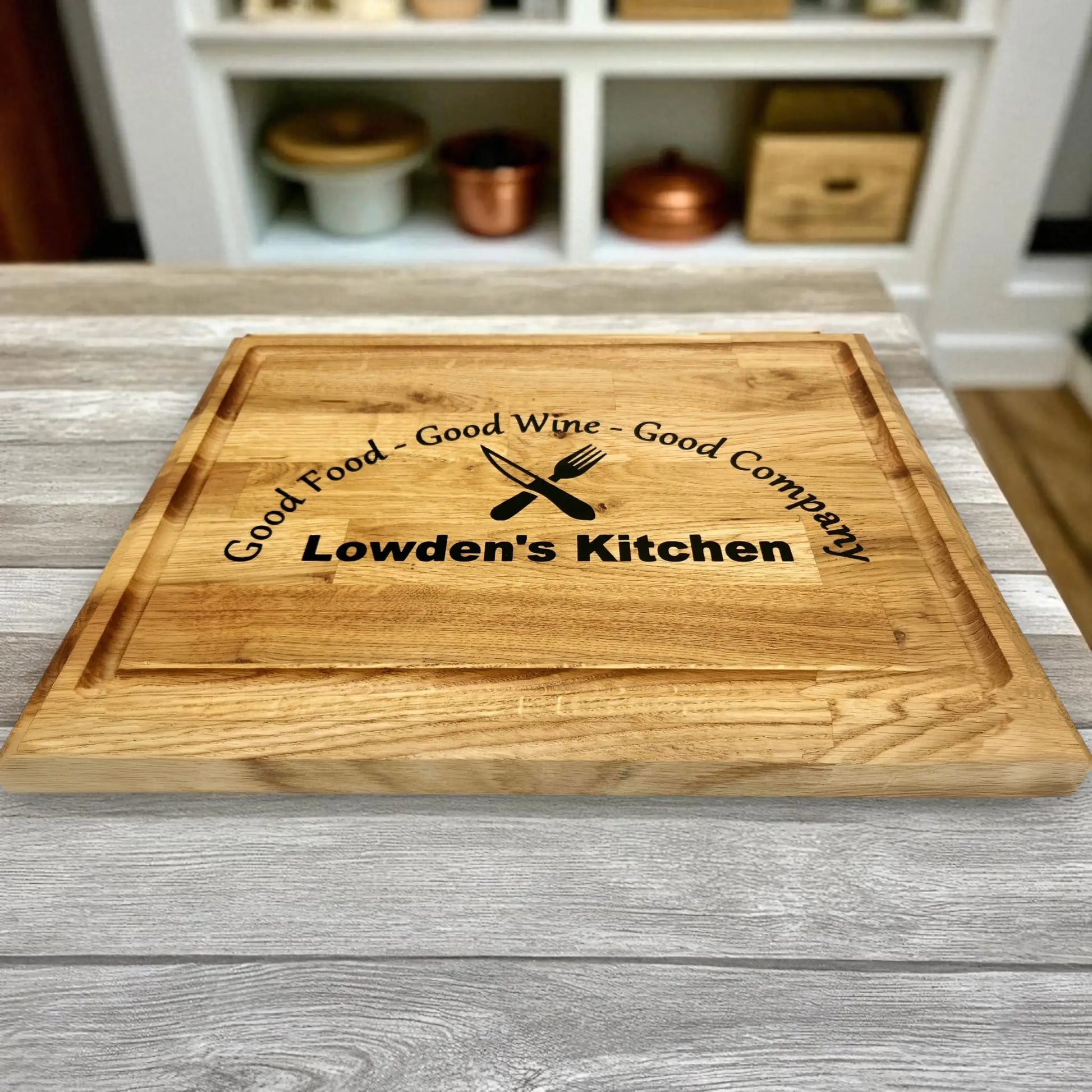 Personalised oak chopping board engraved with the phrase ‘Good Food – Good Wine – Good Company’ and custom name ‘Lowden’s Kitchen,’ displayed on a rustic kitchen counter, ideal gift for home chefs or family kitchens