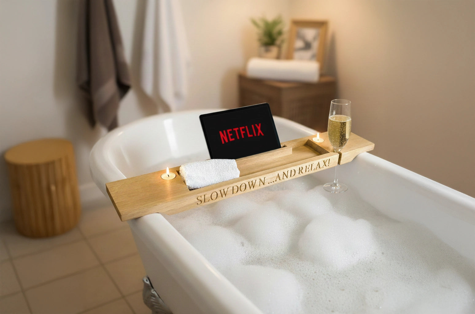 Bath tub with a Netflix on an iPad, glass of wine, and candle on a wooden tray in a bathroom setting.