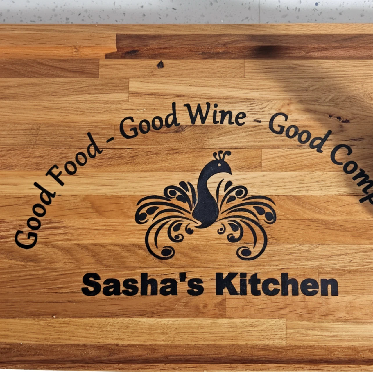 Wooden cutting board with engraved text and logo, featuring 'Good Food - Good Wine - Good Company' and 'Sasha's Kitchen'.