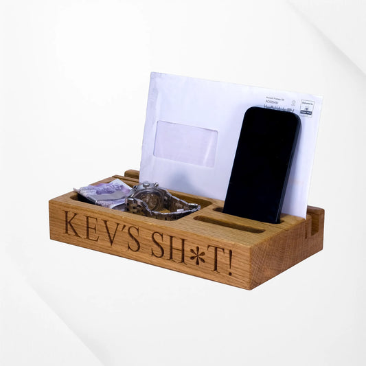 Wooden desk organizer with 'KEV'S SH*T!' engraving, holding a phone, mail, and coins.