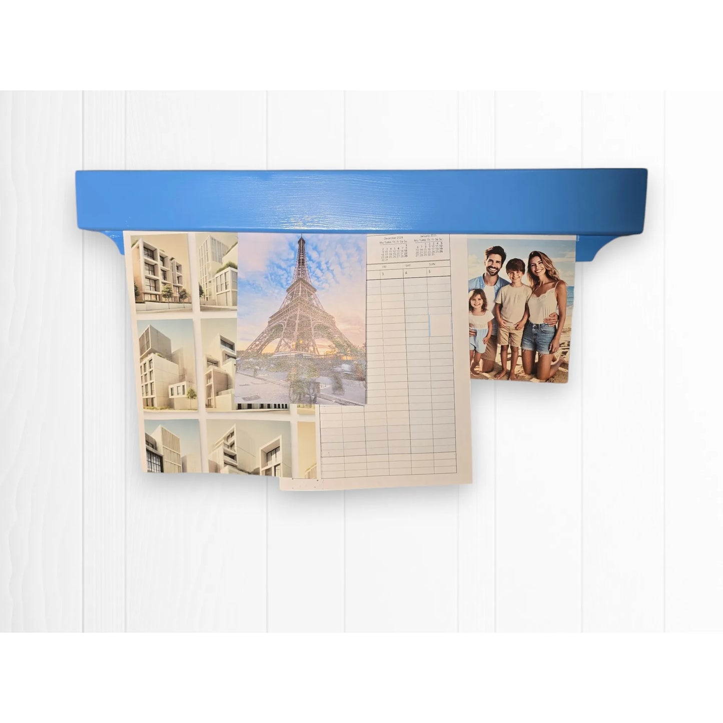 Blue Gravity Track photo and paper holder mounted on a white wall, displaying prints, calendar, and family photo. Colourful wooden display rail, handmade in Cambridge by The Crafty Oak.