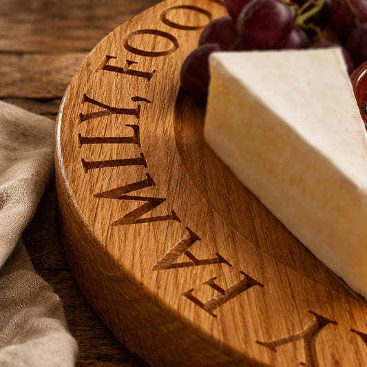 Close-up of a personalised oak cheese board with engraved lettering, styled with cheese and grapes on a rustic wooden table.