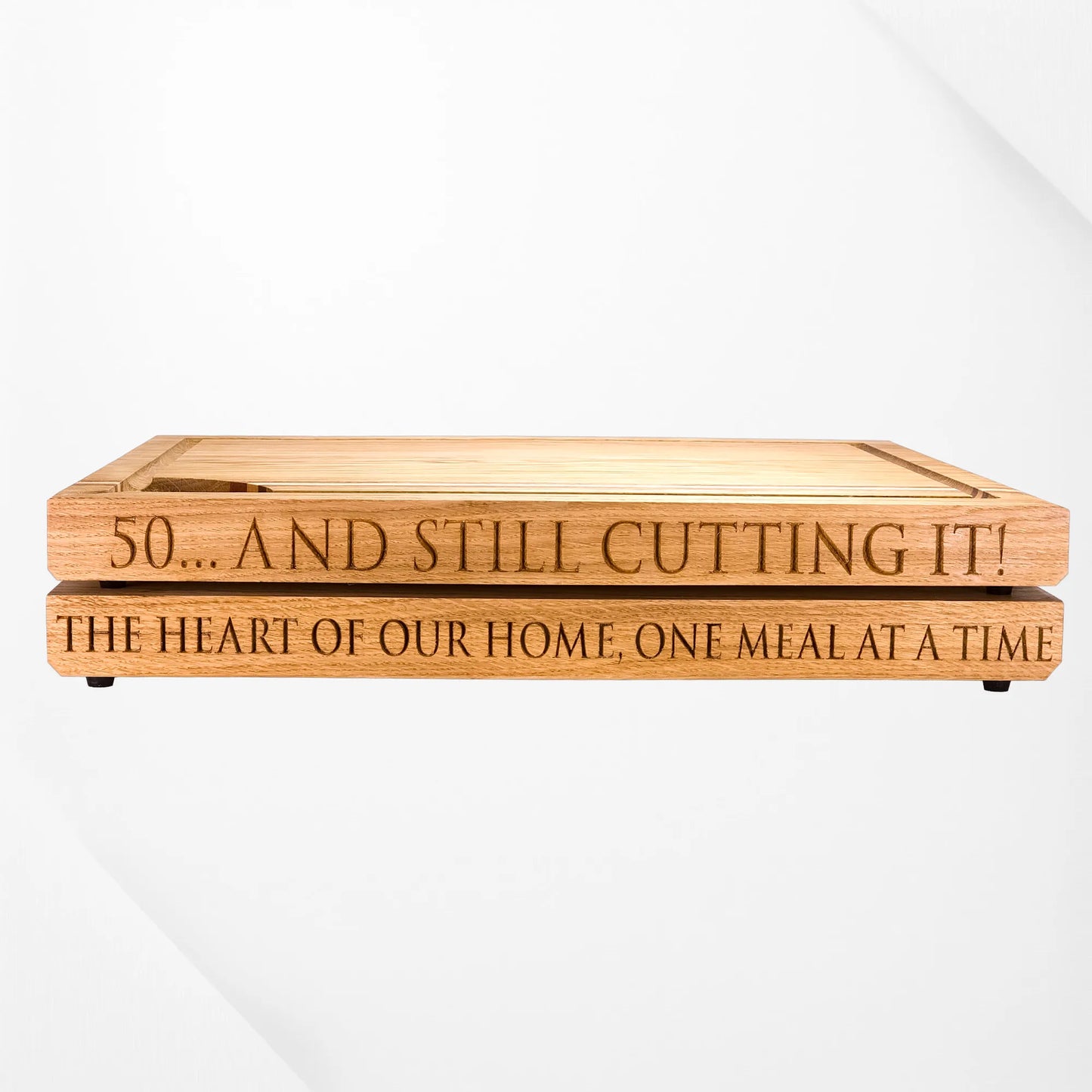 Engraved oak chopping boards with personalised messages, reading “50... and still cutting it!” and “The heart of our home, one meal at a time,” stacked on a white background.