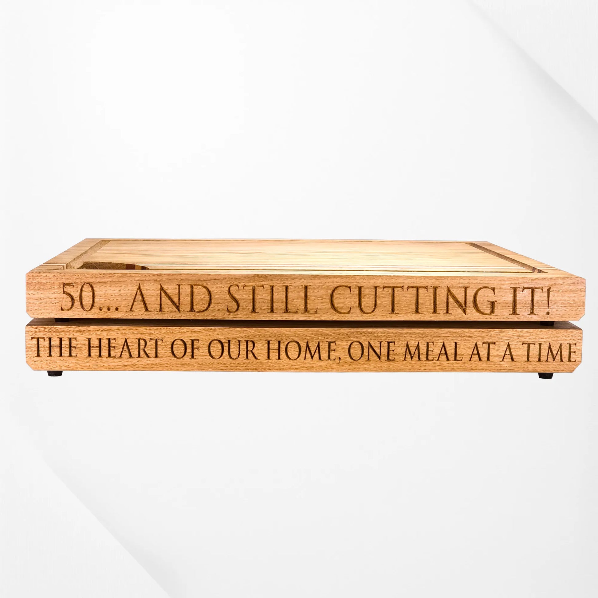 Engraved oak chopping boards with personalised messages, reading “50... and still cutting it!” and “The heart of our home, one meal at a time,” stacked on a white background.