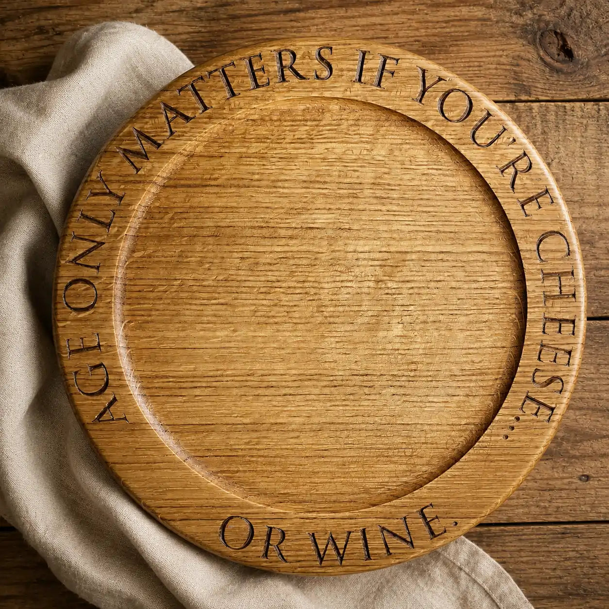 Top-down view of a personalised oak cheese board engraved with “Only matters if you’re cheese. Or wine.”, styled on rustic wood with a linen cloth.
