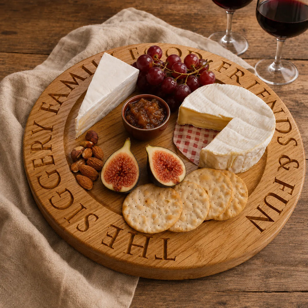 Personalised oak cheese board engraved with custom lettering, styled with cheese, grapes, figs, crackers and chutney on a rustic wooden table.