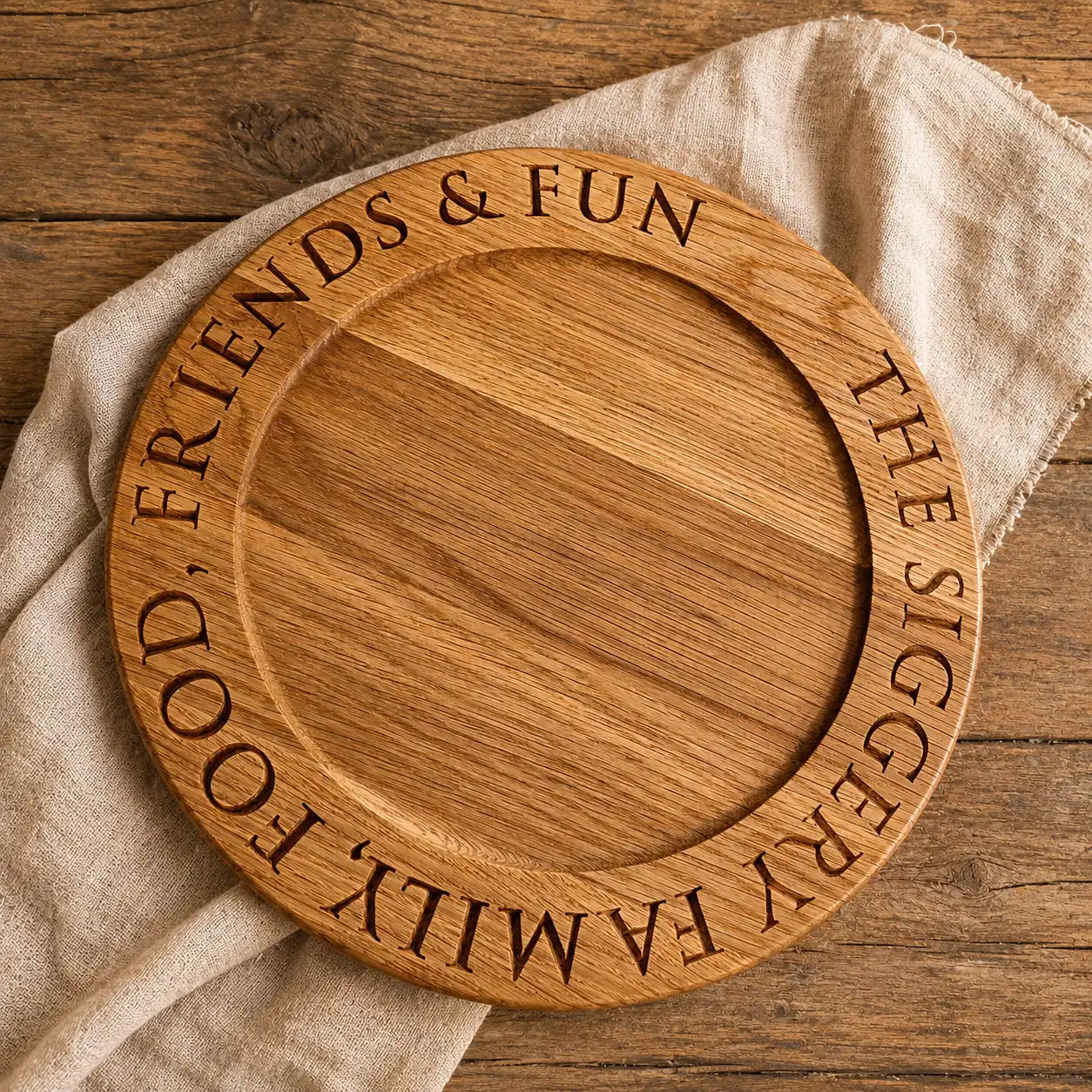 Top-down view of a personalised oak cheese board engraved with “Food, Friends & Fun” and “The Siggery Family”, styled on rustic wood with a linen cloth.