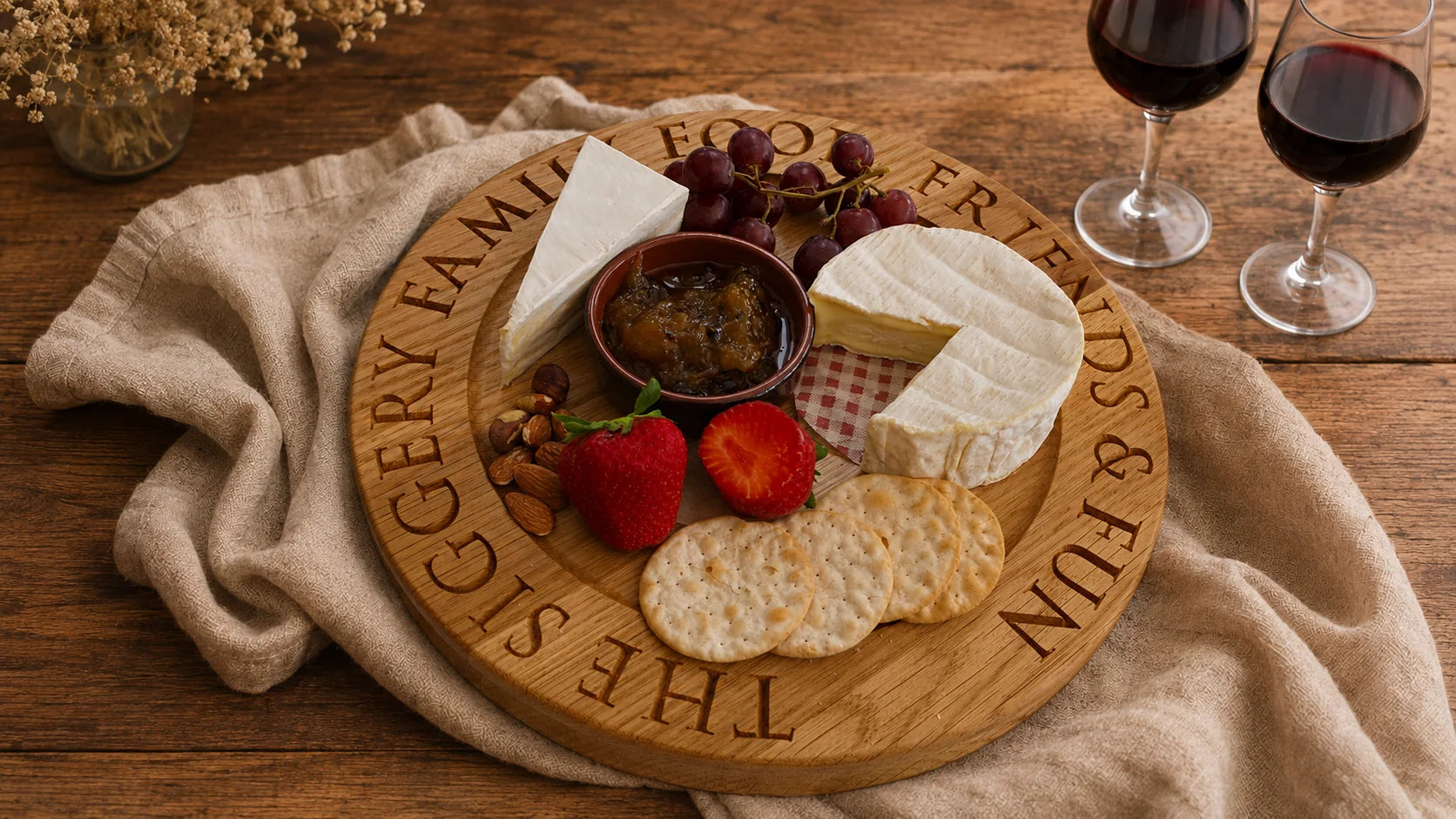 Personalised round oak cheeseboard engraved with a family message, styled with cheese, crackers, fruit and red wine.