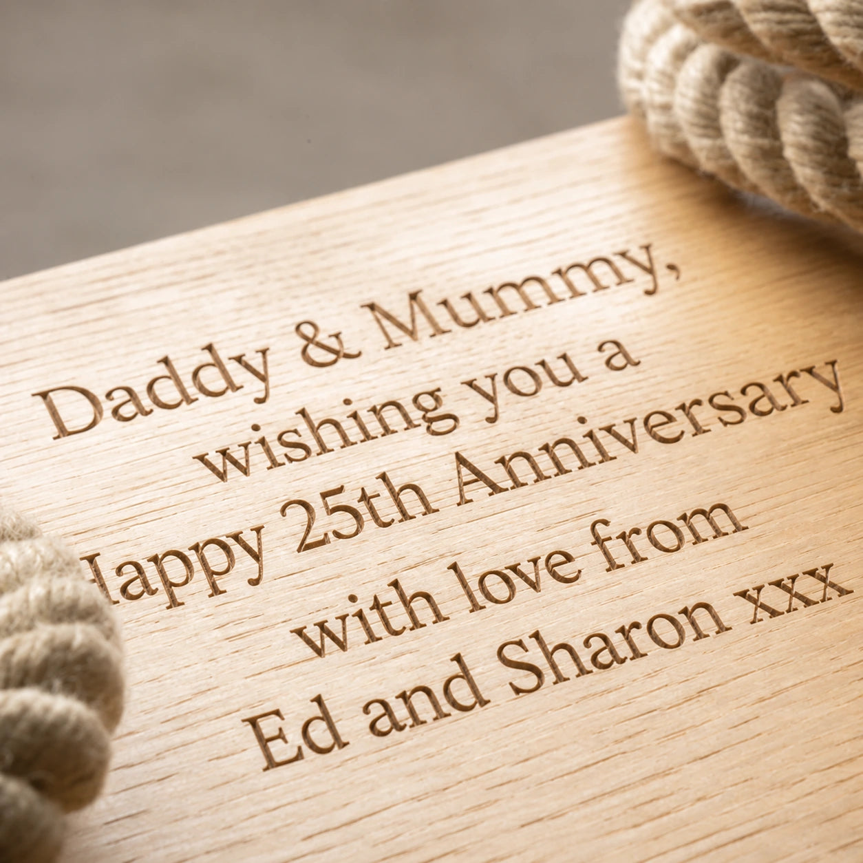 Close-up of a personalised oak rope swing engraved with a 25th anniversary message for Daddy and Mummy.