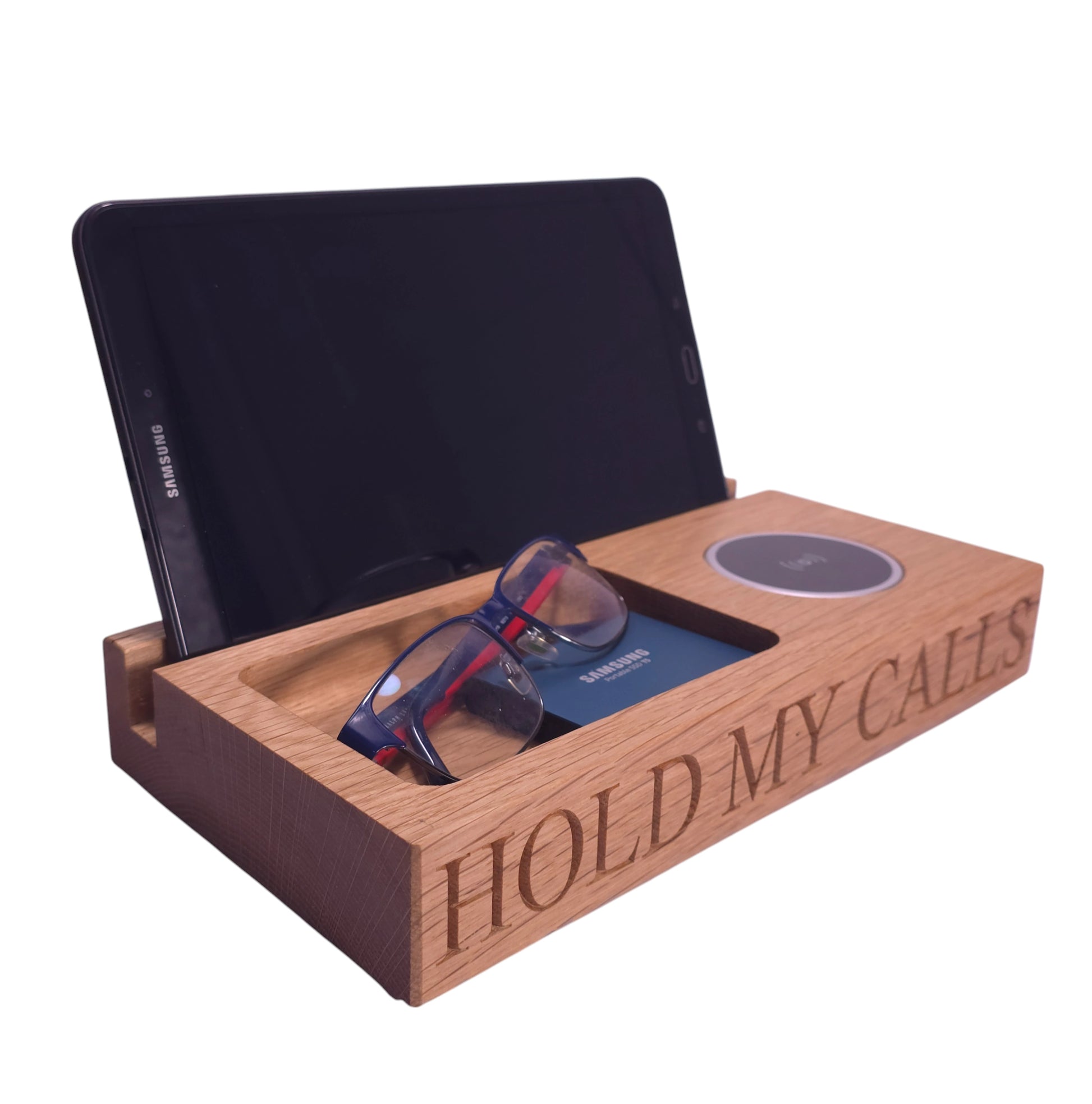 Personalised oak wireless charging tray engraved with ‘Hold My Calls,’ shown with tablet, glasses, and wallet—handcrafted wooden bedside and desk organiser by The Crafty Oak